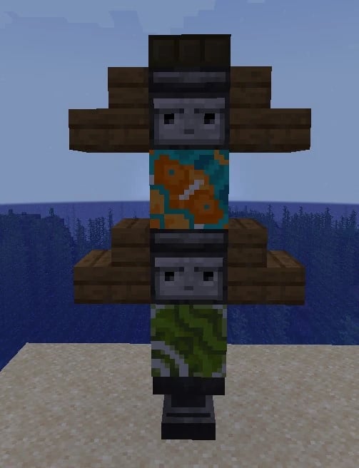 A built Fishing Totem on a beach: two observer faces with dark oak arms, glazed terracotta in between and a stone base